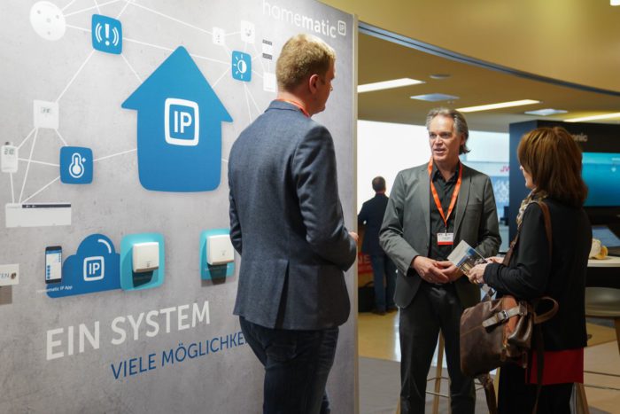 Messestand auf der IFA zum Thema Smart Home. Im Gespräch über IFA-Neuheiten sind zwei Männer und eine Frau. Quelle. Messe Berlin