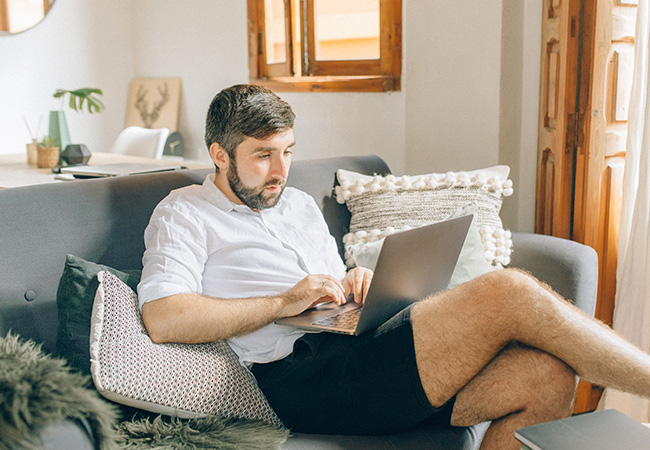 Hybrides Arbeiten: Mann in kurzen Hosen mit einem Laptop auf dem Sofa. Bild: Pexels/Nataliya Vaitkevich