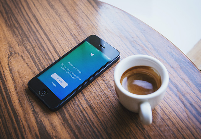 Handy mit Twitter-Startbildschirm auf braunem Holztisch. Daneben eine Kaffeetasse. Bild: Pexels/freestocks.org