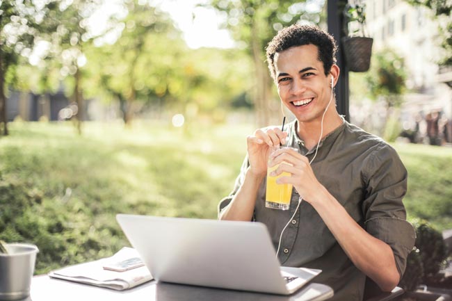 Media Player: fröhlicher Mann mit Orangensaft und Kopfhörern im Park am Laptop. Bild: Pexels/Andrea Piacquadio (https://www.pexels.com/de-de/foto/glucklicher-mann-der-mit-laptop-und-saft-im-park-sitzt-3765030/)