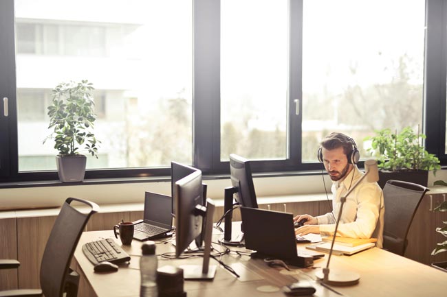 Mann im Büro am Arbeitsplatz mit Kopfhörern. Bild: Pexels/Andrea Piacquadio (https://www.pexels.com/de-de/foto/mann-mit-kopfhorern-gegenuber-computermonitor-845451/)