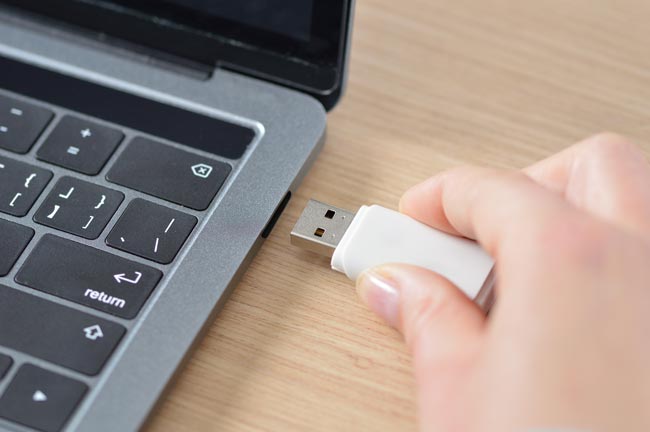 Nahaufnahme einer Hand, die einen weißen USB-Stick an einen Laptop anschließt. Bild: stock.adobe.com/cunaplus (https://stock.adobe.com/de/images/working-with-my-laptop/238973434?asset_id=238973434)