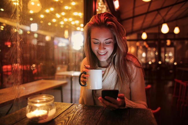 Frau im Café, Becher in der Hand, Blick aufs Handy. Bild: Pexels/Andrea Piacquadio (https://www.pexels.com/de-de/foto/frau-die-weissen-keramikbecher-halt-der-ihr-handy-betrachtet-3783513/)
