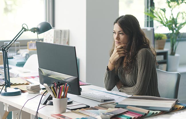 Ordner mit Passwort schützen: Frau am Schreibtisch arbeitet am Computer, sie schaut auf den Bildschirm. Bild: stock.adobe.com/stokkete (https://stock.adobe.com/de/images/young-designer-working-in-her-studio/484117123?asset_id=484117123)