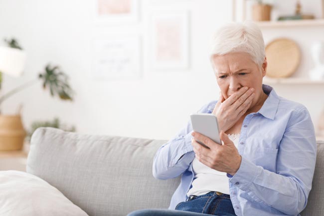 Erschrockene Seniorin blickt auf Ihr Handy. Bild: stock.adobe.com/Prostock-studio (https://stock.adobe.com/de/images/worried-senior-lady-reading-shocking-news-on-smartphone-at-home/360430095?asset_id=360430095)