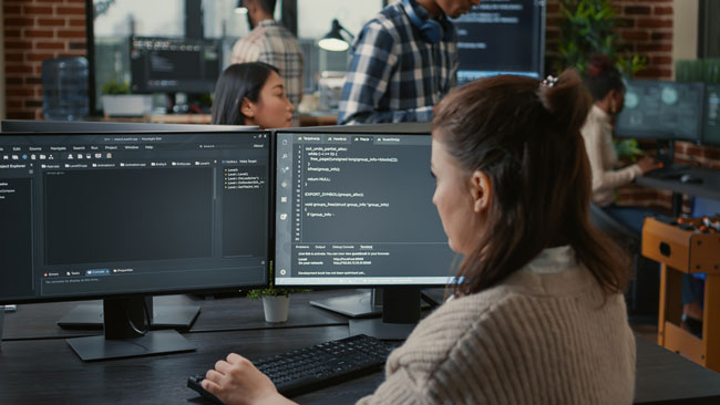 Büro mit Computern mit mehreren Mitarbeitern. Bild: stock.adobe.com/ DC Studio https://stock.adobe.com/de/images/software-programer-writing-code-in-front-of-multiple-computer-screens-displaying-artificial-intelligence-algorithm-developer-coding-database-while-colleagues-doing-online-cloud-computing/487959586