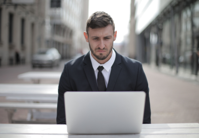 Bundeslagebild Cybercrime 2025: Mann sitzt im Anzug draußen vor seinem Laptop und schaut betrübt. Bild: Pexels/ Andrea Piacquadio
