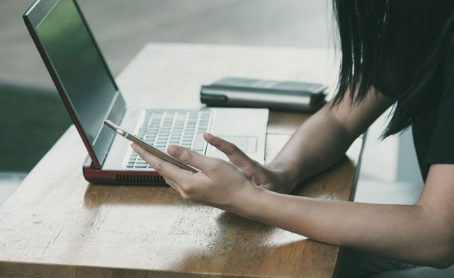 Person am PC lässt sich vom Handy ablenken. E-Mail-Angst am Arbeitsplatz. Bild: Pexels/Porapak Apichodilok https://www.pexels.com/de-de/foto/frau-die-auf-stuhl-neben-tisch-sitzt-wahrend-sie-telefon-benutzt-363766/