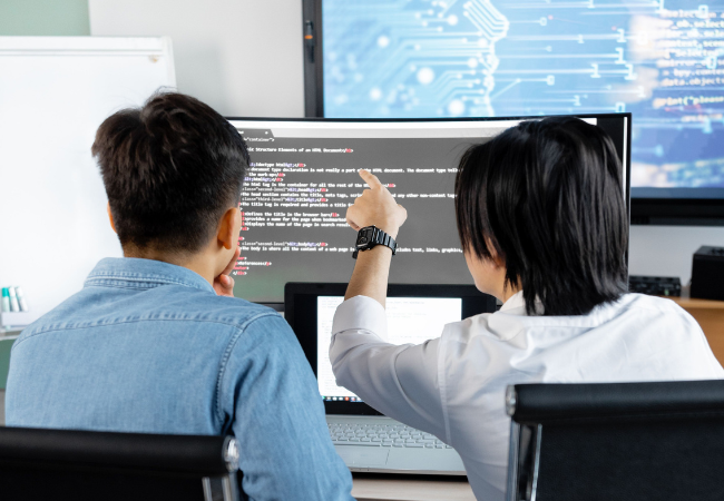Kontextbasierte Priorisierung entlastet IT-Teams gezielt und senkt so Kosten und Reaktionszeiten und mindert so die Alert Fatigue. Zu sehen sind zwei ITler, die vor einem Bildschirm sitzen. Bild: Pexels/ Mikhail Nilov https://www.pexels.com/de-de/foto/menschen-buro-manner-sitzung-7988759/