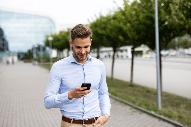 Gemini deaktivieren: Ein gutaussehender Geschäftsmann, der sein Smartphone benutzt und lächelt. Ein fröhlicher junger Mann, der Apps auf seinem Handy nutzt, Bild: stock.adobe.com/YURII MASLAK https://stock.adobe.com/de/images/handsome-businessman-using-smartphone-and-smiling-happy-young-man-using-mobile-phone-apps-texting-message-browsing-internet-looking-at-smartphone-young-people-working-with-mobile-devices/385265366